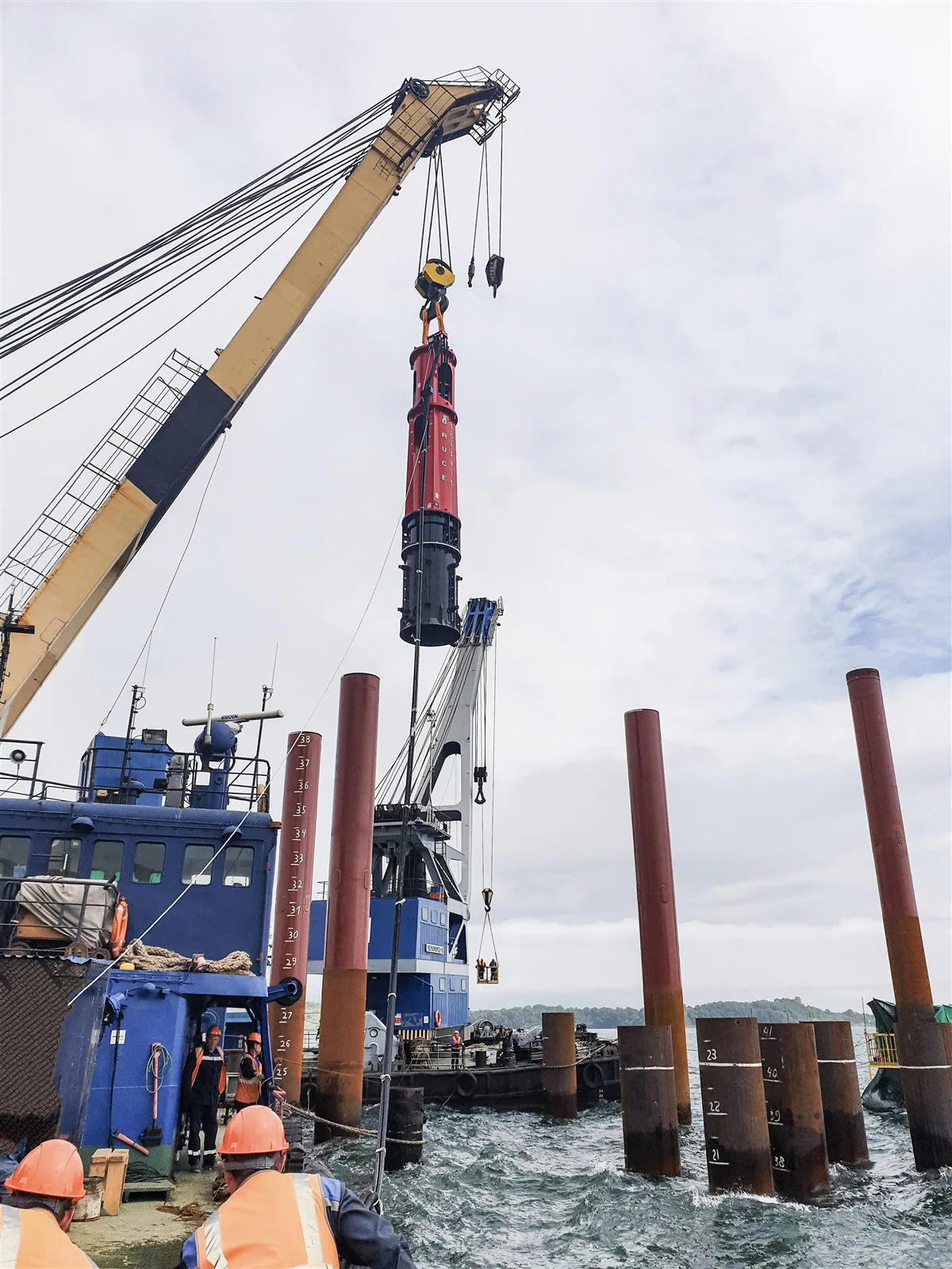 BRUCE hydraulic impact hammer suspended above a vessel work area beside tubular piles