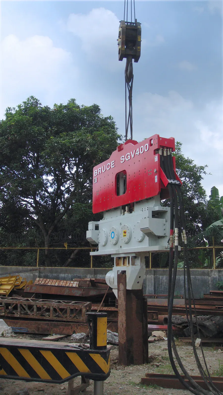 BRUCE SGV400 vibratory hammer suspended at a worksite, with crane rigging, steel pile and hydraulic hoses