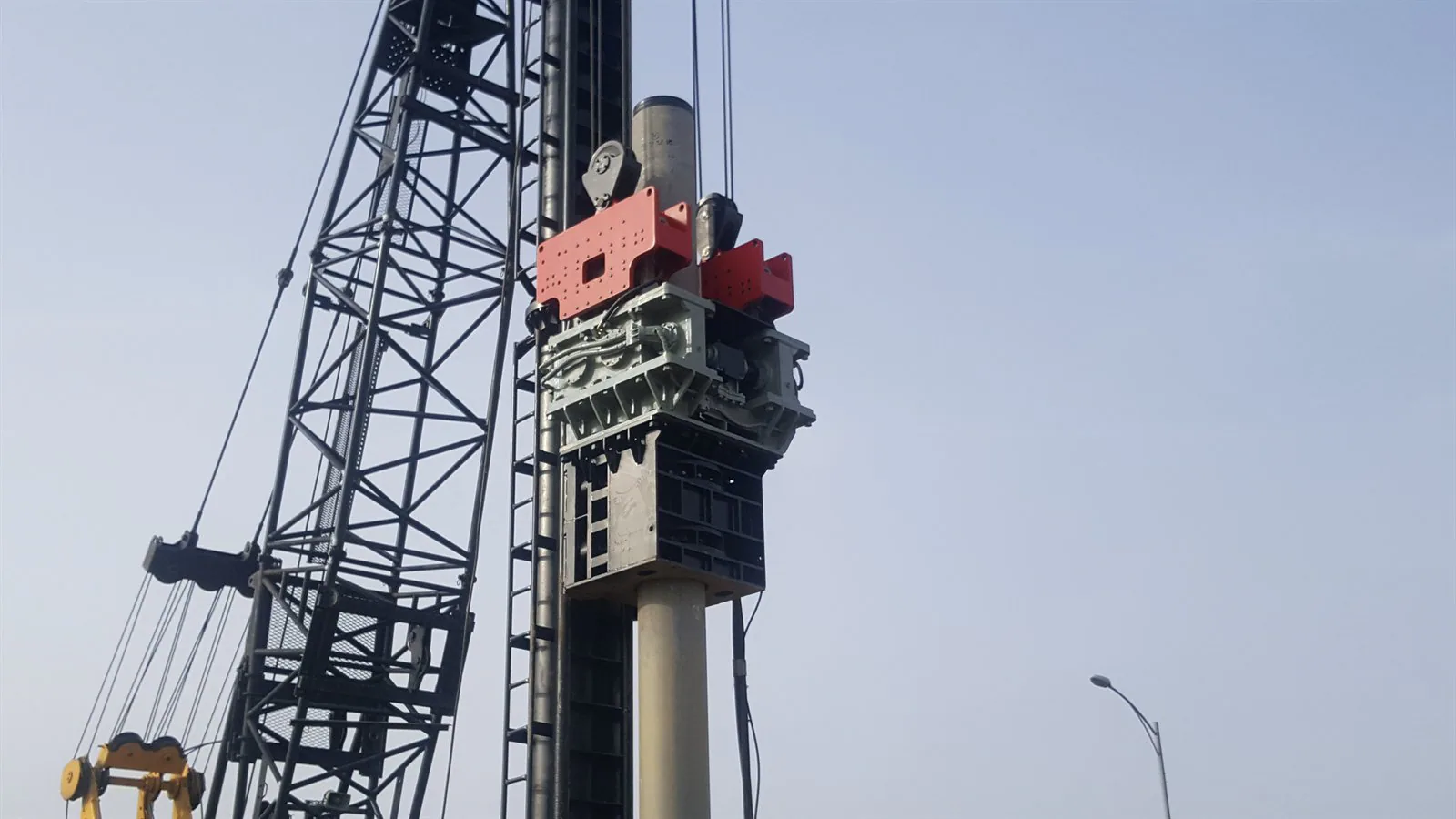 BRUCE vibratory hammer positioned around a cylindrical pile, with crane lines and hydraulic hoses